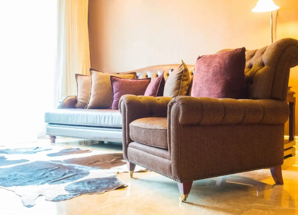 A close-up of a richly textured brown armchair and a leather sofa in a well-lit living room, representing household furniture that can be moved using the uses of utility trailers.